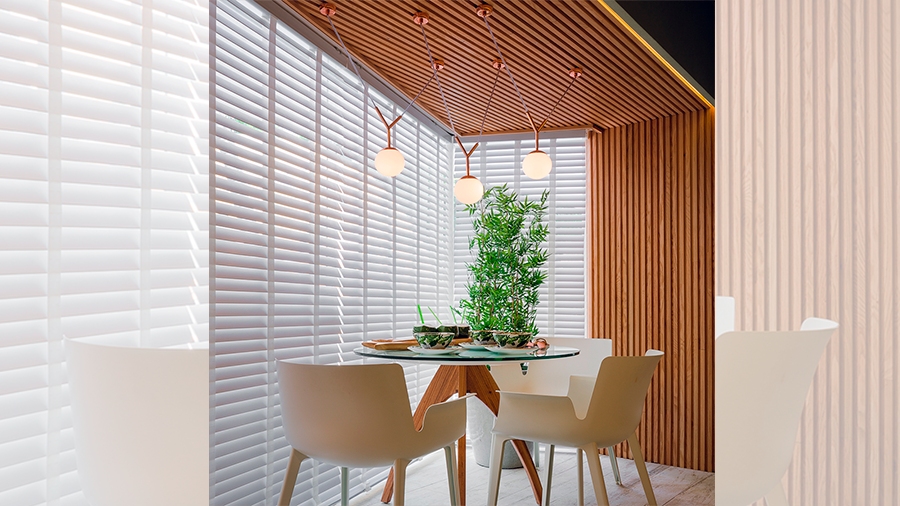 Fotografia de um sala de jantar com parede revestida em brise de madeira, mesa, cadeiras, plantas e utensílios de cozinha