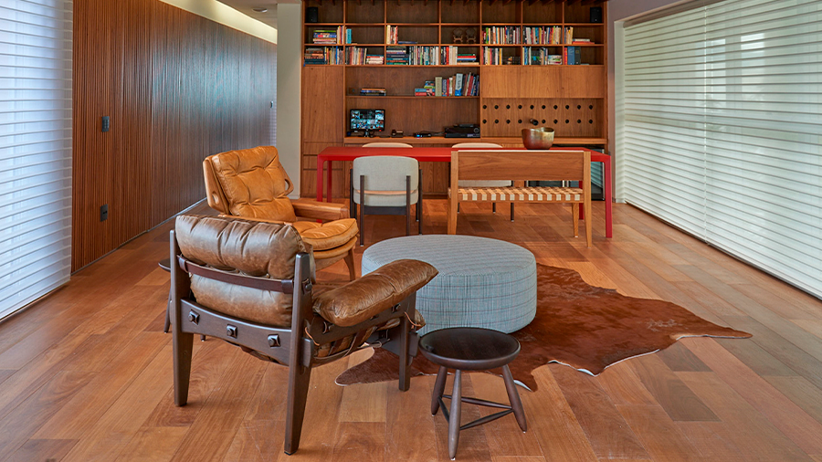 escritório com estilo rústico, com destaque para o pisos e revestimentos de parede, mesa marrom centralizada, poltrona em primeiro plano, todos os móveis em marrom. 