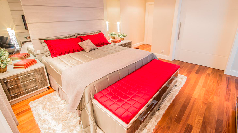 Quarto com piso de madeira em tom médio, cama com decoração vermelho e branco e decoração do quarto predominante branco.