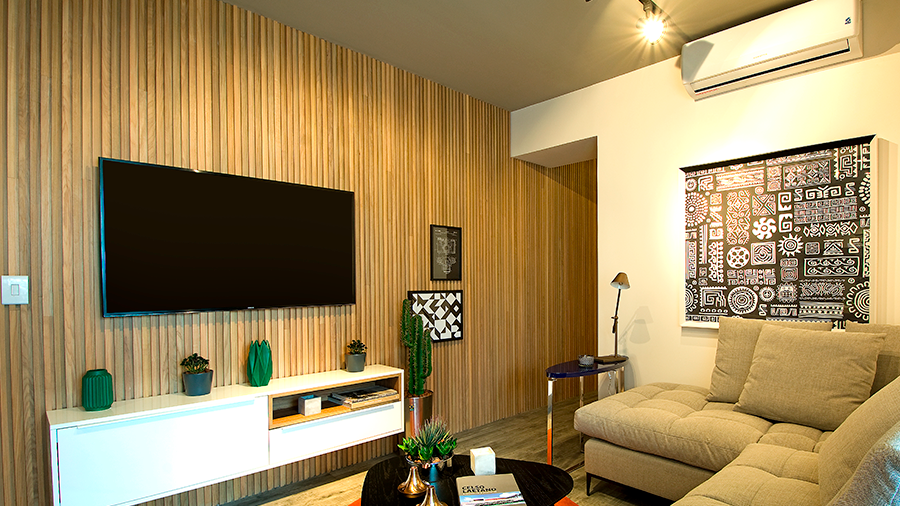 Imagem de uma sala com sofá bege, mesa de centro, rack suspenso na parede, TV, quadros e parede de madeira Brise Tauari.