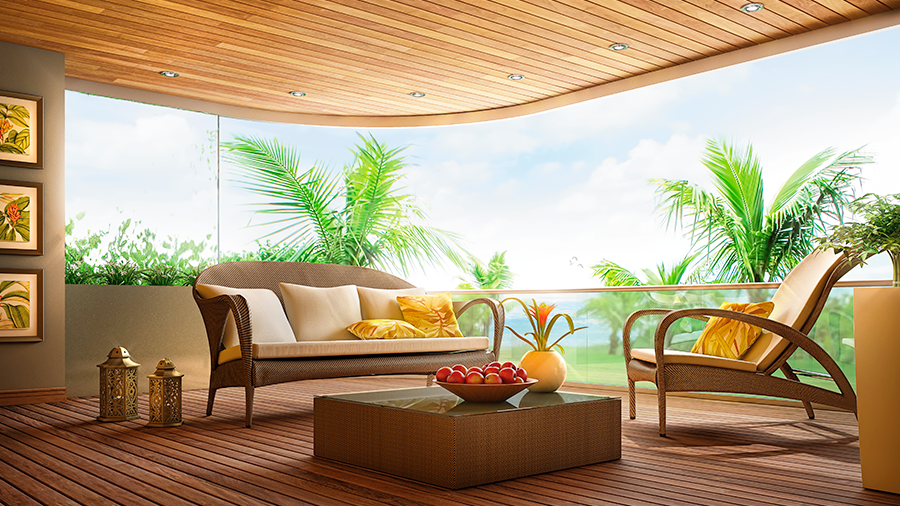 Imagem de um ambiente com teto e deck de madeira, um sofá e uma poltrona claros com almofadas, além de uma mesa de centro com vasos. Do lado de fora, há diversos coqueiros.
