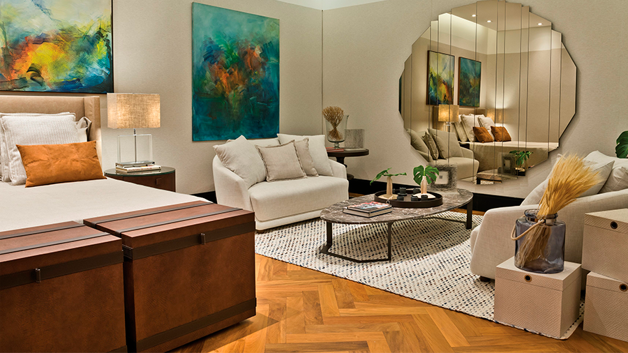 Quarto com sofás para ambiente de leitura, piso de madeira Peroba, espelho redondo e quadros abstratos ao fundo.