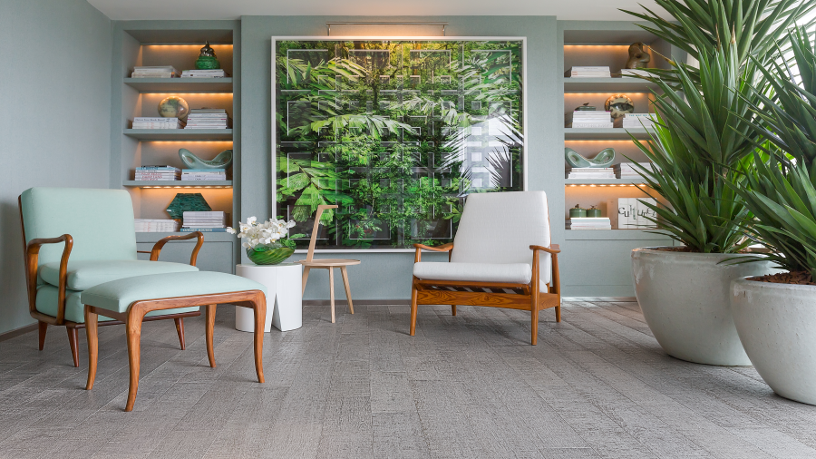 Ambiente de descanso com poltronas, piso de madeira cinza e decoração em tons de branco e verde