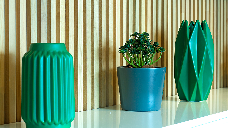 Imagem de uma estante branca com dois armários verdes, um vaso com uma planta no centro, e a parede revestida de madeira Brise.