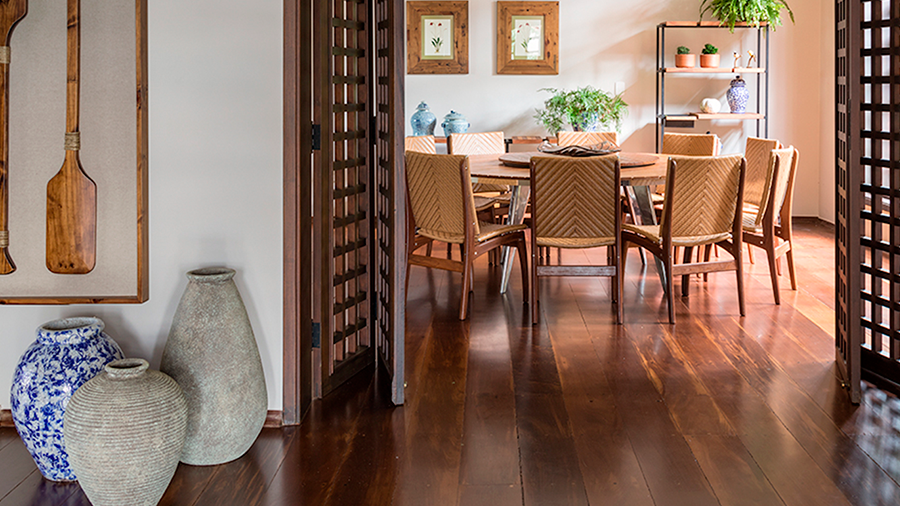  Fotografia de um espaço interno com piso de madeira, mesa de jantar, cadeiras, vasos e demais objetos de decoração.