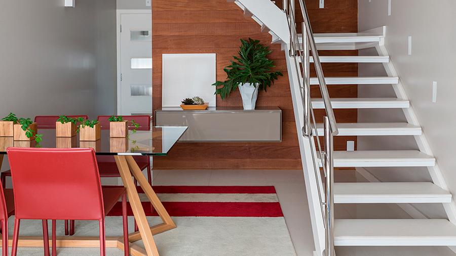  Fotografia de um espaço interno com revestimento de parede de madeira, piso de cerâmica, escada branca, mesa de jantar, cadeiras e objetos de decoração.