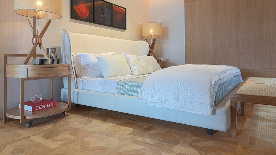 Fotografia de um quarto com piso e móveis de madeira, luminárias e cama de casal.