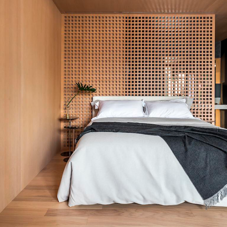 Fotografia de um quarto com piso de madeira, cama de casal e uma divisória de madeira.