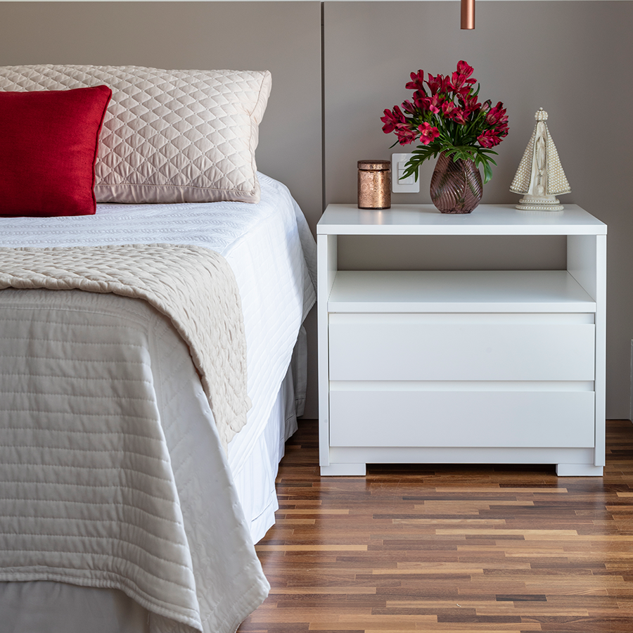 otografia de um quarto com piso de madeira, mesa de cabeceira branca, cama de casal e itens de decoração.