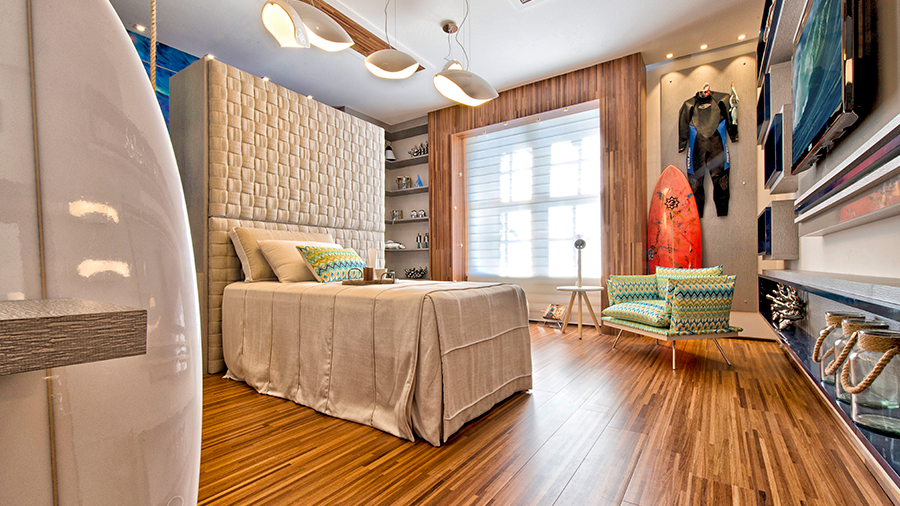 Fotografia de um quarto com piso de madeira, cama de solteiro, luminária de teto, poltrona verde e itens de decoração.