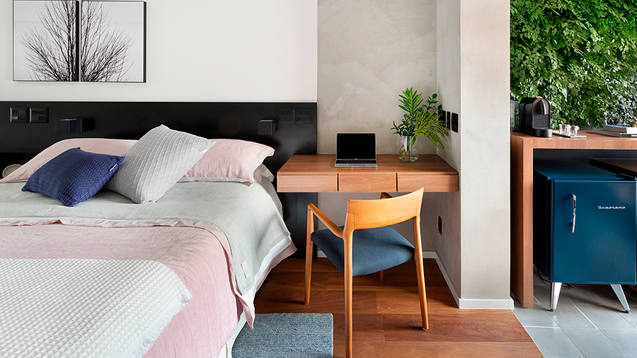 Fotografia de um quarto com piso de madeira, cama de casal, escrivaninha e cadeira de madeira e itens de decoração.