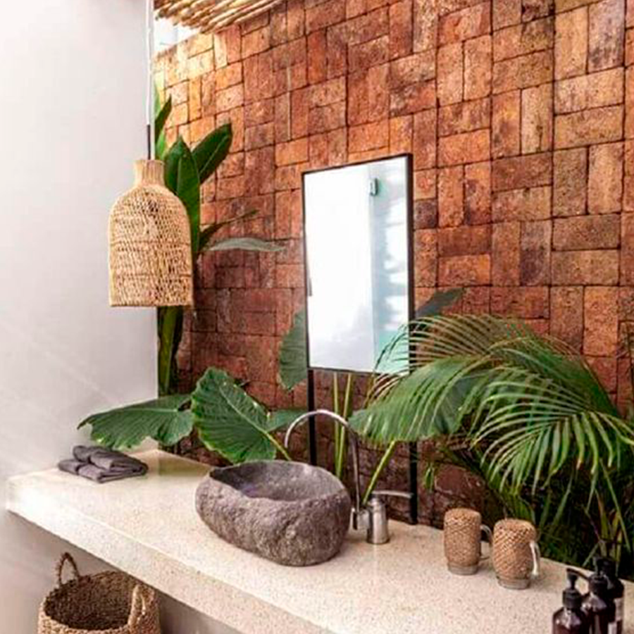 Banheiro com foco na parede e cubra de pedra, com decorações em palha e plantas. 