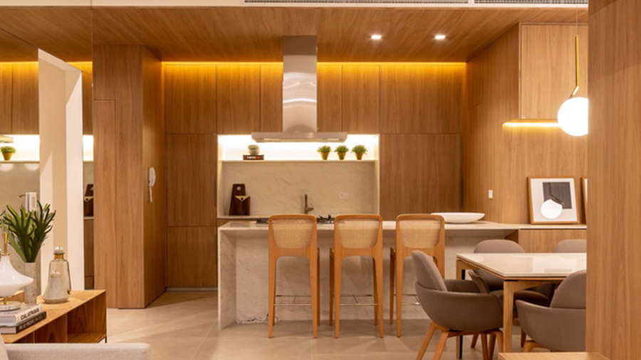 Fotografia de cozinha integrada, com piso e revestimento de madeira, móveis amadeirados e iluminação pendente.