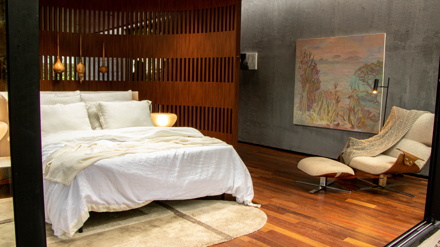 Fotografia de quarto composto por piso de madeira, cama de casal, iluminação pendente e divisória de madeira.