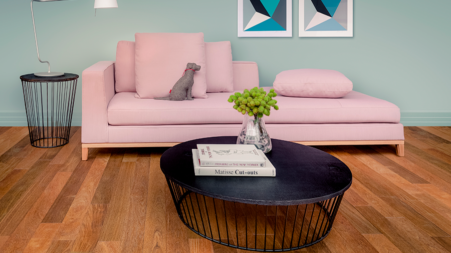 Fotografia de sofá rosa, mesa de centro com livros e vaso de vidro, mesa lateral e piso assoalho de madeira