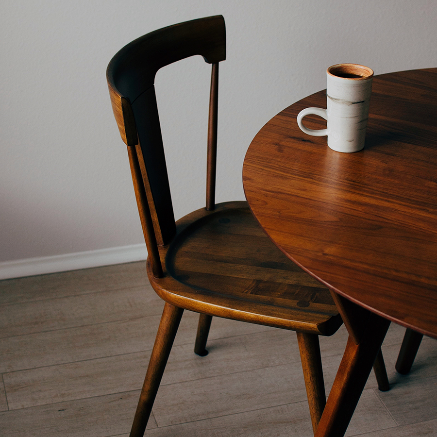Fotografia de mesa e cadeira em tons quentes de madeira e piso de madeira em cor fria.