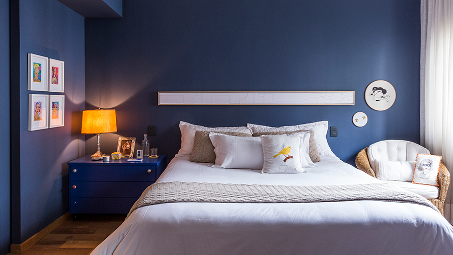 Fotografia de um quarto com paredes e móveis azuis, cama de casal e piso de madeira.