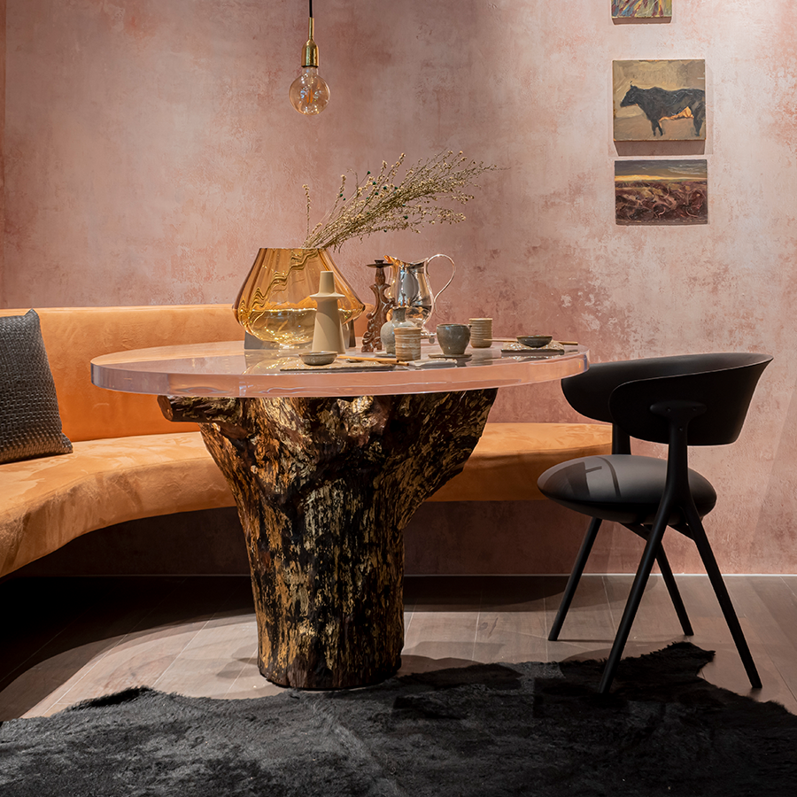 Fotografia de um ambiente interno com sofá, poltrona, tapete e uma mesa de tronco de madeira com tampo de vidro. 