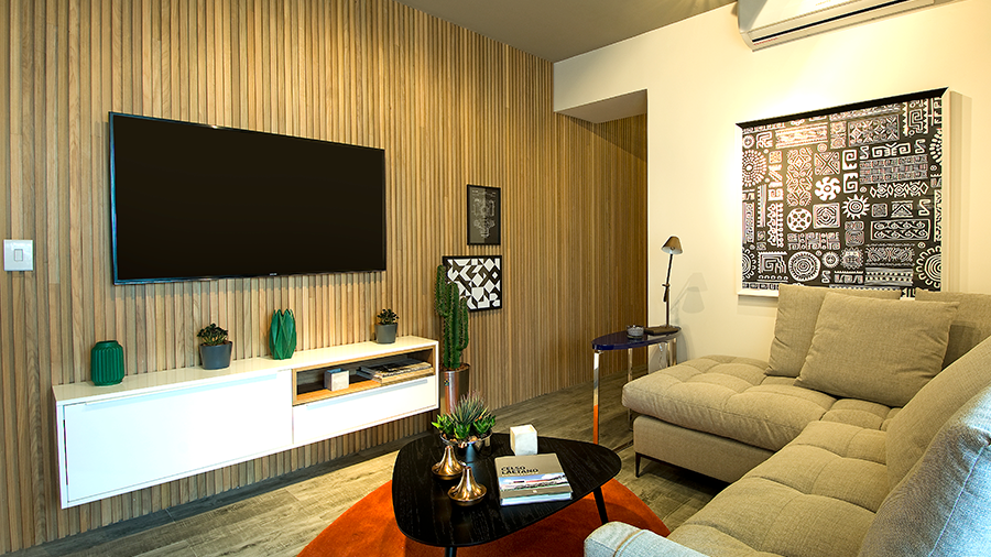 Fotografia de um ambiente interno com painel ripado de madeira, televisão e móveis de sala de estar.