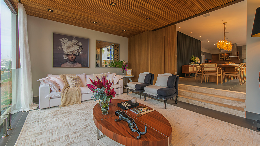Fotografia de um espaço integrado entre sala de estar e jantar com divisória de brise de madeira, mesa de centro de madeira, móveis de cores neutras, tapete bege e itens de decoração.
