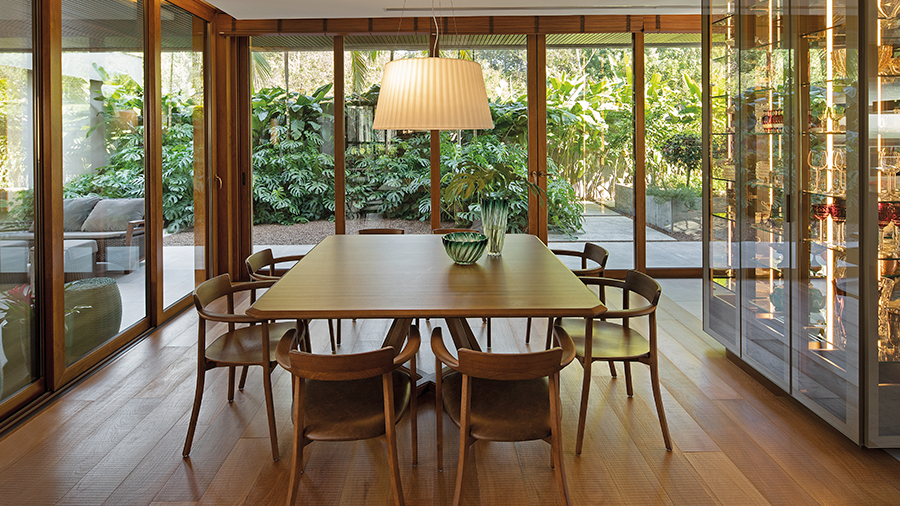 Fotografia de sala de jantar com piso e móveis de madeira com vista para varanda grande quantidade de plantas.