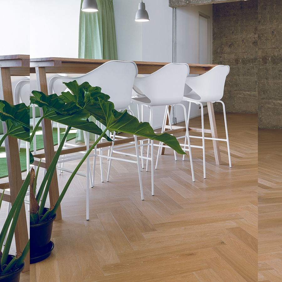  Fotografia de espaço corporativo com piso de madeira, mesas alta de madeira, bancos altos brancos e um vaso de planta.