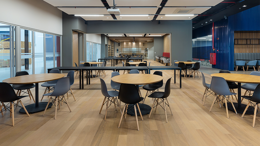  Fotografia de espaço corporativo com piso de madeira e mesas e cadeiras de madeira com detalhes pretos.