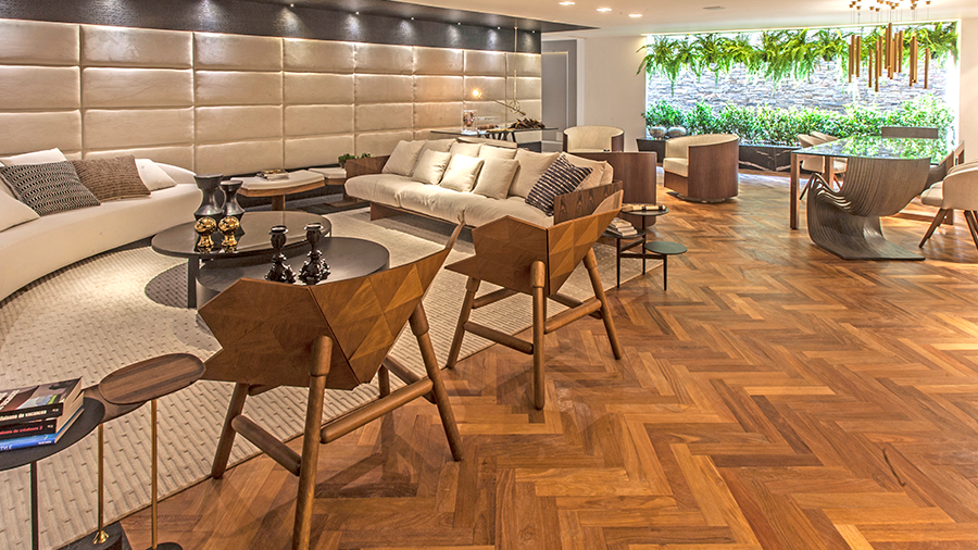 Fotografia de uma sala de estar com piso de taco de madeira na cor escura, móveis de madeira e itens de decoração.