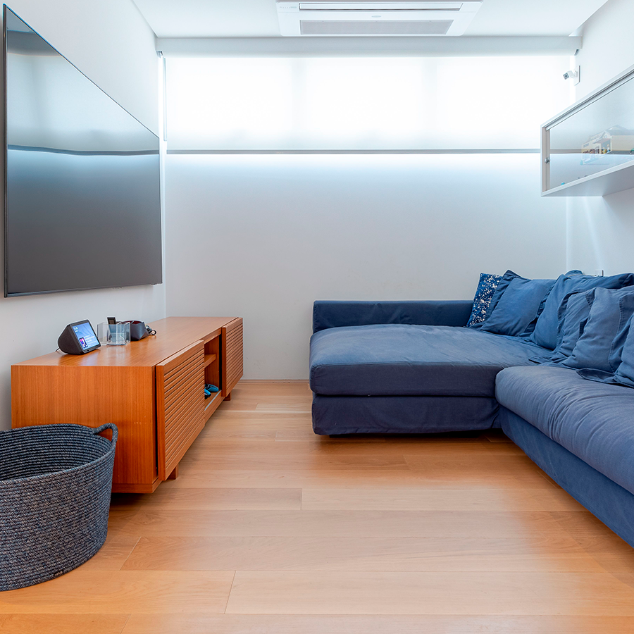 sala de estar com sofá azul, rack e televisão compõe o espaço. 