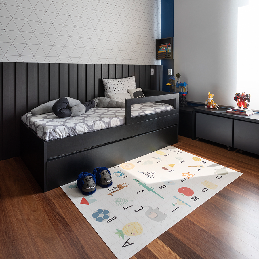 quarto infantil com design moderno, uso de preto em painel, cama de solteiro e bancadas, decoração com tapete interativo e brinquedos. 