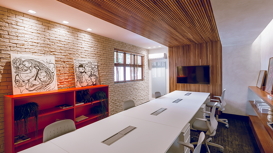 Fotografia de um ambiente de trabalho com parede e teto revestidos de brise de madeira, uma grande mesa com estações de trabalho, móveis e elementos de decoração.