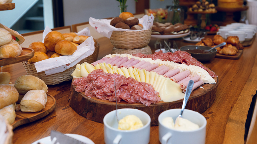 Fotografia de uma mesa de brunch com pães e frios.