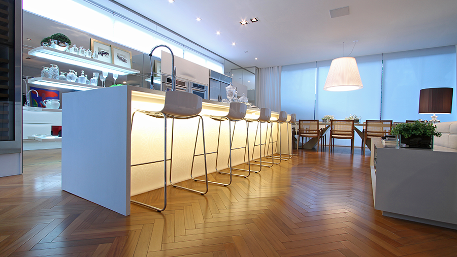 Fotografia de uma cozinha com piso de madeira, bancada central, móveis e luminárias