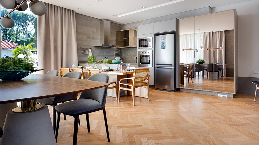 Fotografia de uma cozinha com piso de madeira, duas mesas, eletrodomésticos e utensílios.