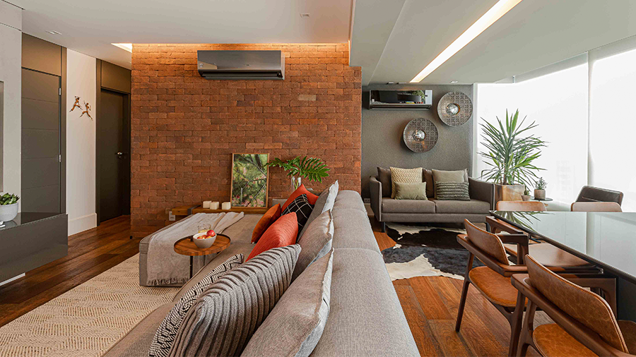 Ambiente integrado de sala de estar e sala de jantar, com piso de madeira, parede 'estilo tijolinhos' e decoração com tecidos confortáveis e aconchegantes