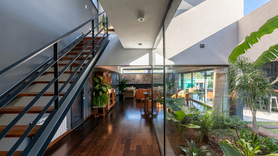 Fotografia de um espaço interno com piso de madeira sucupira, escada e jardim