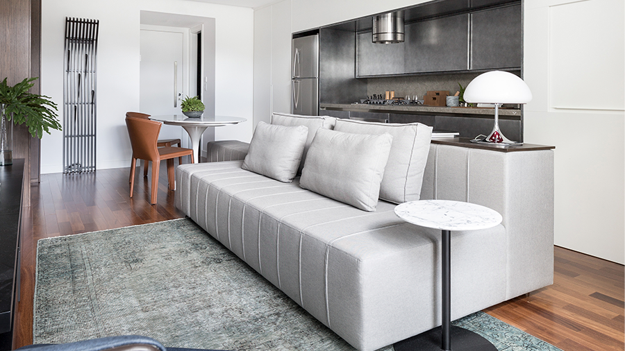 Fotografia de um uma sala de estar com piso de madeira, sofá e tapete cinza, móveis e objetos de decoração