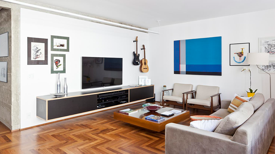 Fotografia de um uma sala de estar com piso de madeira, sofá cinza, mesa de centro, rack suspenso, televisão, móveis e objetos de decoração