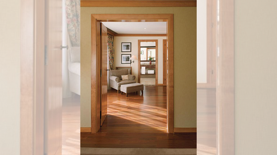 Fotografia da entrada de um quarto de hotel com piso de madeira, poltrona cinza com apoio de pé, quadro e objetos de decorações