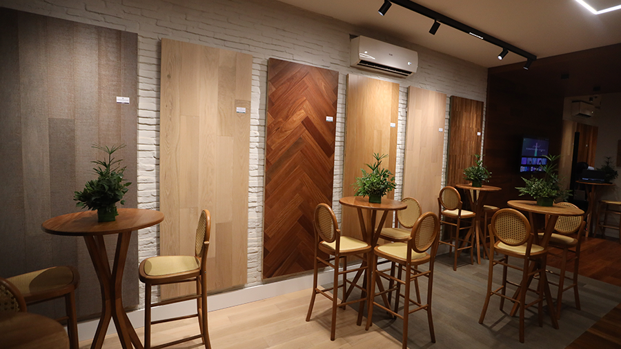 Mesas e cadeiras de madeira e amostras de pisos de madeira de diversas tonalidades na parede ao fundo