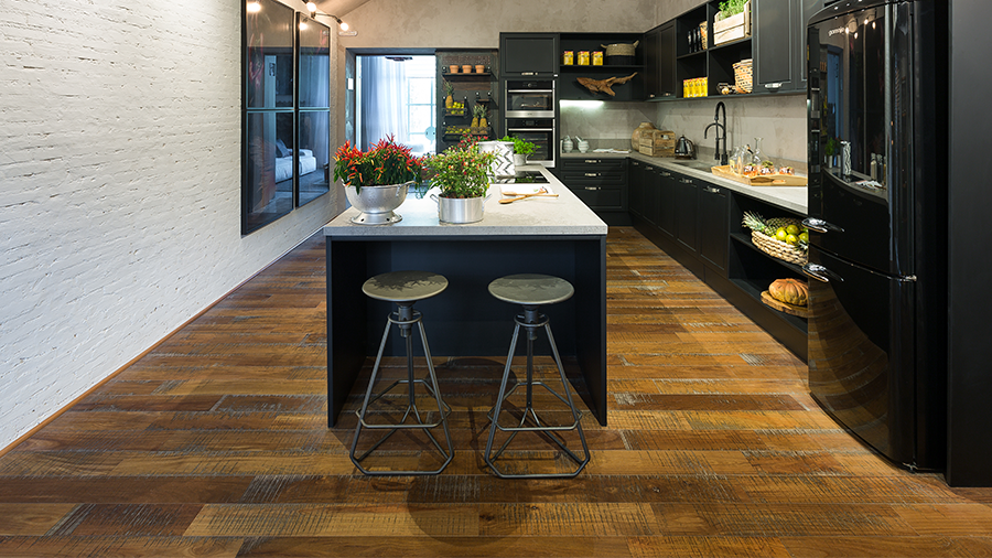 Cozinha com piso de madeira e móveis pretos, paredes claras e iluminação estilo industrial
