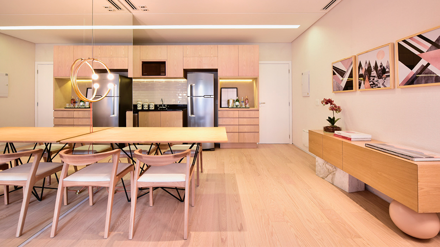 Cozinha utilizando tons de branco e creme nos móveis e decoração, piso de madeira claro e quadros preto, rosa e branco na parede lateral.