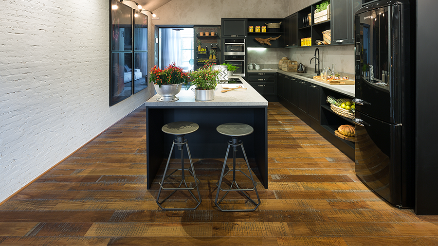 Cozinha com piso de madeira, parede de cimento queimado, móveis preto, ilha com mármore claro no centro.