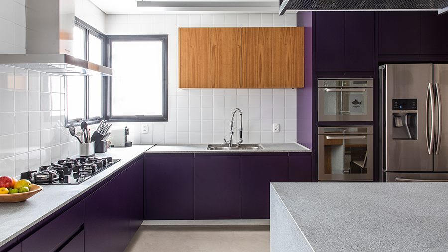 Imagem de uma cozinha com estilo industrial, apresentando uma ilha rodeada de armários na cor roxa e eletrodomésticos, com o armário na parte superior em madeira.