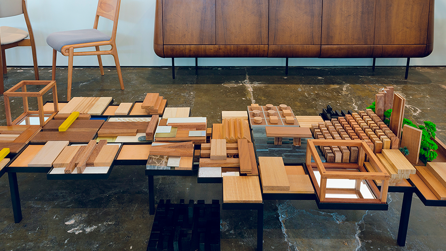 Imagem de uma peça com vários tipos e formatos de madeira, lançada em parceria com o Plataforma4 e a Indusparquet. Ao fundo, um armário de madeira e duas cadeiras.