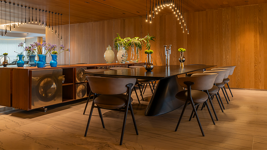 Imagem de uma sala com uma mesa de madeira cercada por cadeiras, adornada com vasos. Ao lado, um aparador de madeira com objetos decorativos, e um pendente para sala de jantar.