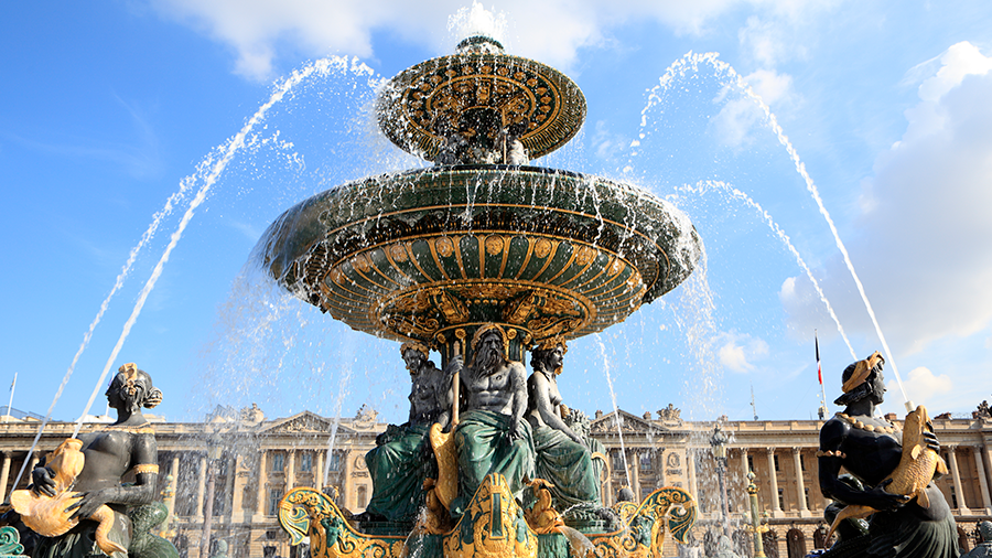  Imagem da Fonte dos Mares na Praça da Concórdia, exibindo uma arquitetura neoclássica, com um grande chafariz em tons de verde e amarelo, contendo duas esculturas pretas e amarelas em seu interior.
