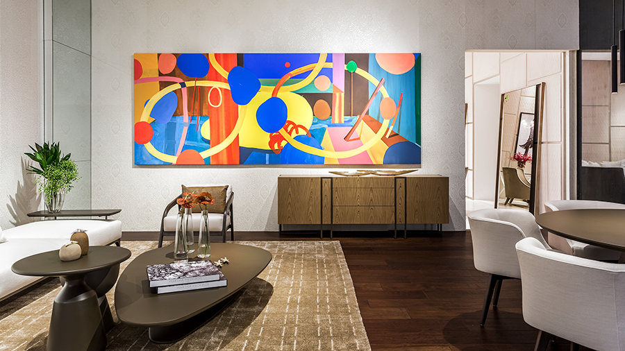 Imagem de um espaço com decoração retrô, com assoalho de madeira multiestruturado, um tapete com mesas de centro decoradas, um armário ao fundo com um quadro colorido acima e duas poltronas nas laterais.