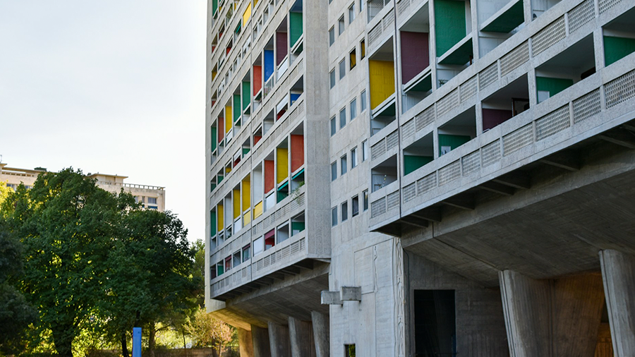 Prédio Unités d'Habitation, com cimento a mostra e diversas janelas coloridas, na lateral da imagem é possível ver uma árvore em um jardim