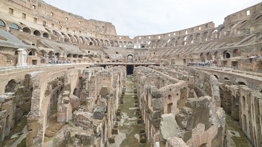 Imagem da arena do Coliseu com diversas pedras no centro e uma estrutura grande ao redor formando um círculo.